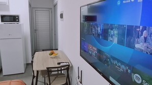Eine kleine, moderne Küche mit einer Mikrowelle und einem Kühlschrank, ein Essbereich mit Tisch und Stühlen sowie ein großer Flachbildfernseher an der Wand, der verschiedene Streaming-Dienste anzeigt.