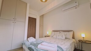 A bedroom with a bed, nightstands, a wardrobe, and an air conditioning unit. - 83 Lim3 - Stay Sunlit Apartment (Limassol)