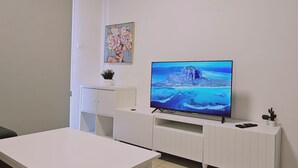 Ένα σύγχρονο σαλόνι με τηλεόραση επίπεδης οθόνης, λευκά έπιπλα και μια μονάδα κλιματισμού.