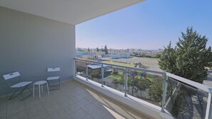 A balcony with two chairs and a table, overlooking a playground and buildings.