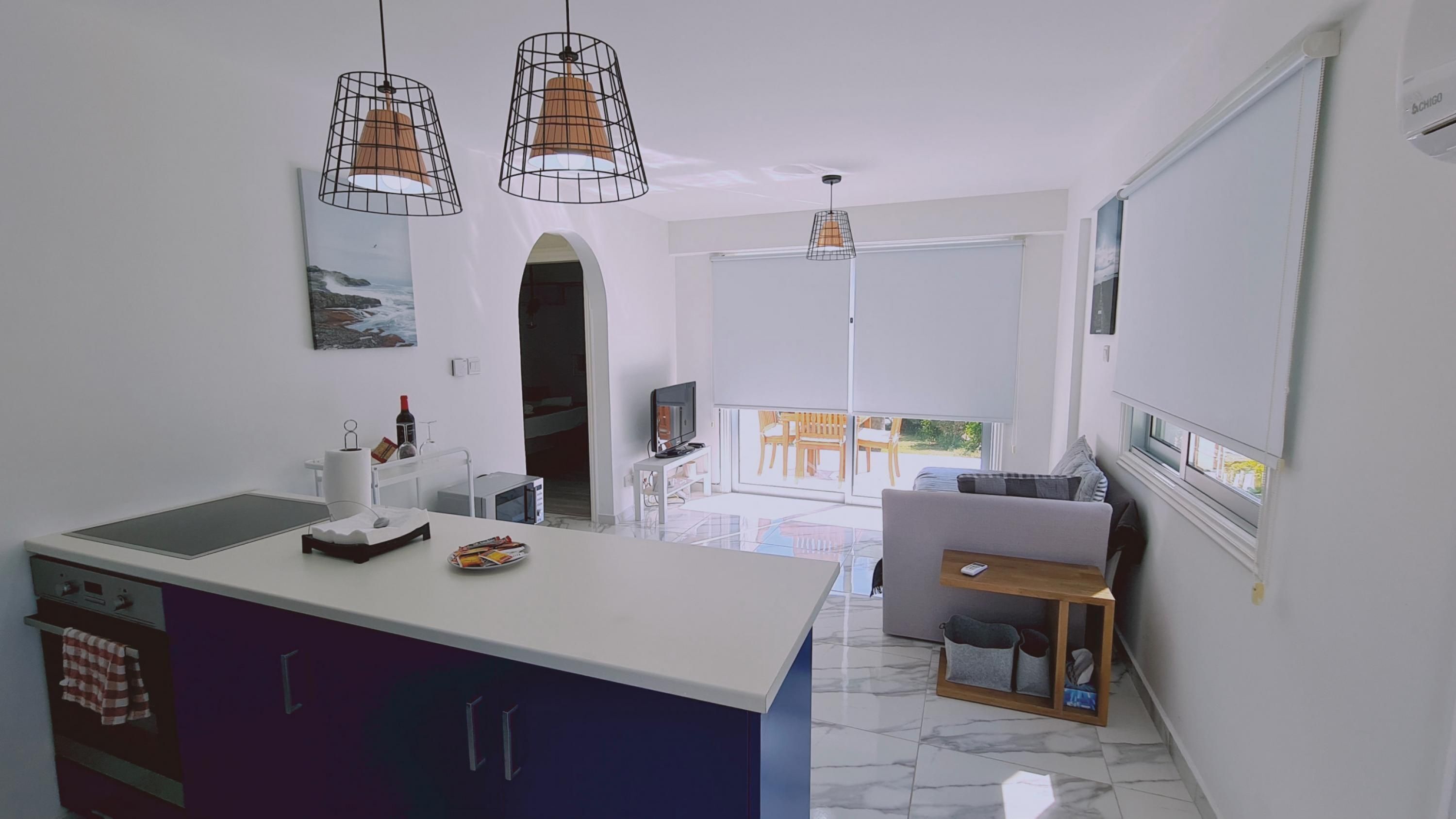 Une cuisine moderne dotée d’un îlot central, un coin repas avec une table et des chaises, et un espace de vie comprenant un canapé et un téléviseur.