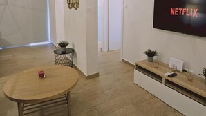 Moderni olohuone, jossa on puinen ruokapöytä, seinälle asennettu televisio, jossa näkyy Netflix, ja minimalistinen sisustus.