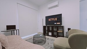 Un saló amb una televisió que mostra 'NETFLIX', un ordinador portàtil sobre una taula, un sofà i un armari amb objectes decoratius.