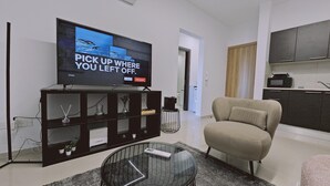 Un saló modern amb un televisor de pantalla plana, un sofà, una taula de cafè de vidre i una cuina al fons.
