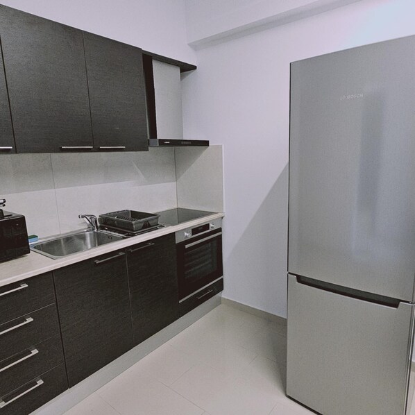 A modern kitchen with dark cabinets, a stainless steel sink, and a large refrigerator. - 104 NIC - 402 Stay Cosmo City Suite (Nicosia)