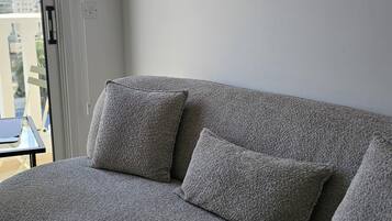 A grey sofa with two cushions in a room with a large window.