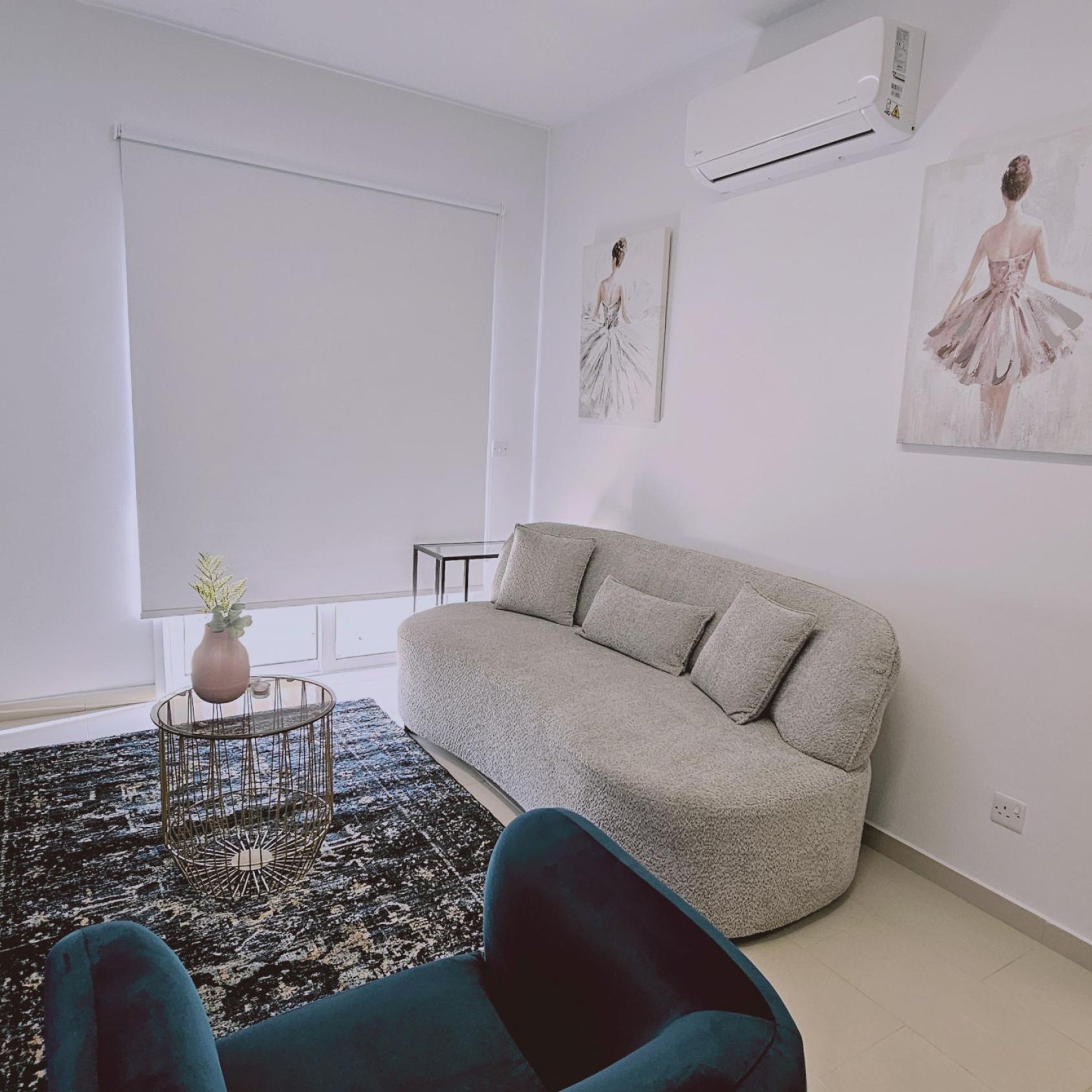 Ein Wohnzimmer mit einem grauen Sofa, einem kleinen runden Tisch mit Pflanze und zwei Wand-Klimaanlagen.