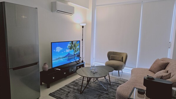 A modern living room with a flat-screen TV, a sofa, a coffee table, a chair, and a refrigerator. - 104 NIC - 102 Stay Cosmo City Suite (Nicosia)