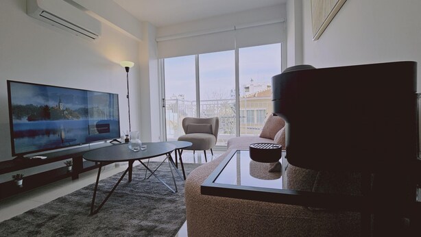 Una sala de estar moderna con un televisor de pantalla plana grande, una mesa de centro de vidrio, un sofá y una silla.