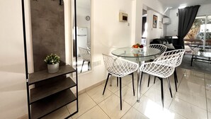 Een moderne eetruimte met een glazen tafel en witte stoelen, een kleine potplant en een zwart metalen plank.