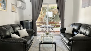 Een woonkamer met twee zwarte leren banken, een glazen salontafel en een balkon met een tafel en stoelen.