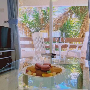 Ein Esstisch mit Glasplatte, darauf ein Teller mit Keksen und Macarons, ein weißer Stuhl und links daneben ein Fernseher auf einem Schrank.