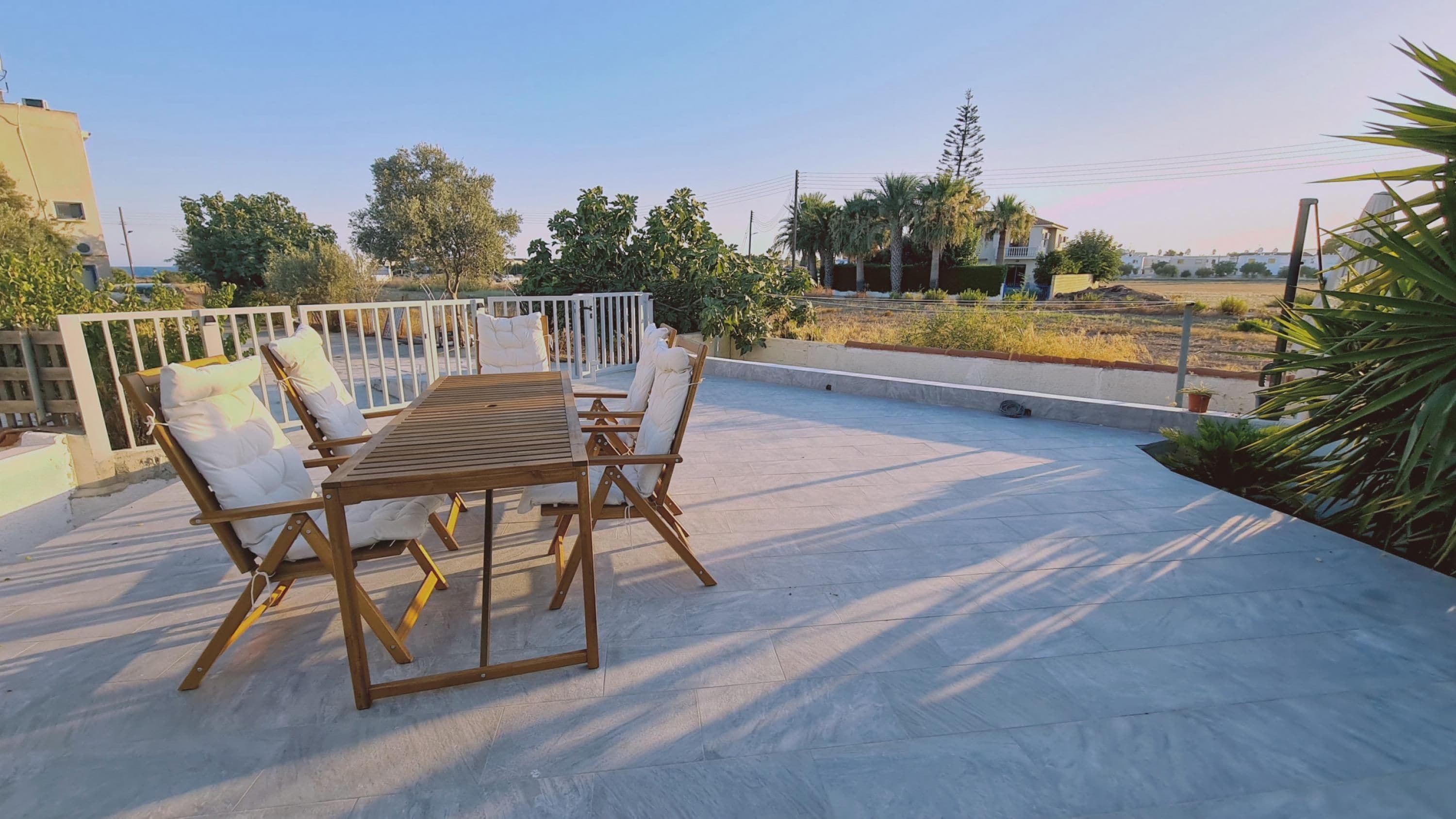 A rooftop terrace with a wooden table and chairs, surrounded by a white railing.
