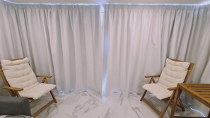 Une pièce avec deux chaises en bois et une petite table, un sol en marbre et une grande fenêtre avec des rideaux.