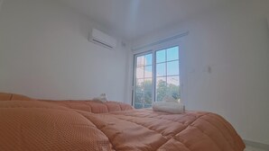 Een slaapkamer met een groot raam, een airconditioning en een bed met een gebreid plaid.