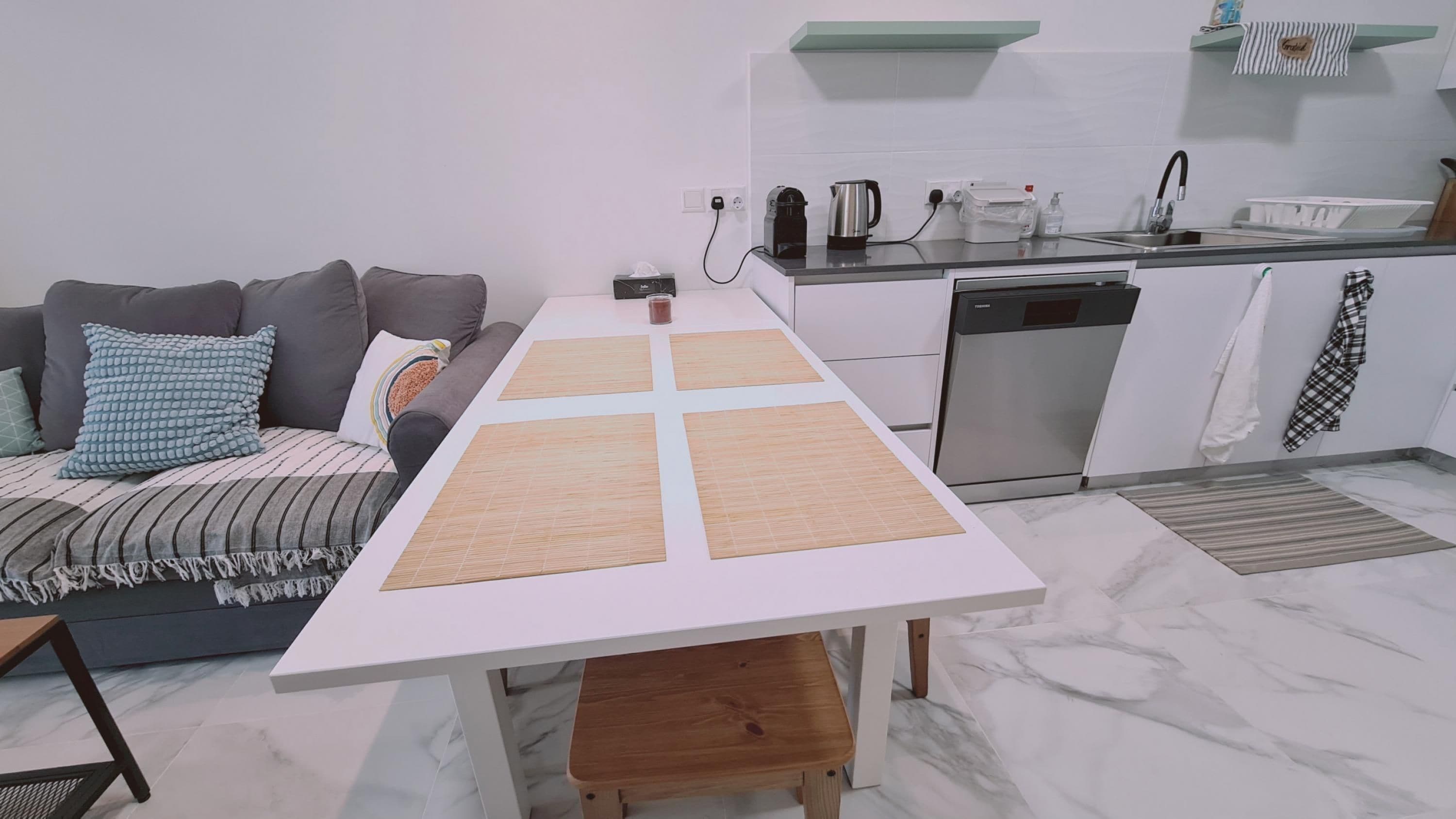 A modern kitchen with a dining table, sofa, and a dishwasher.