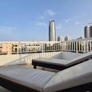 Une terrasse sur le toit, dotée de chaises longues et offrant une vue sur les immeubles modernes.