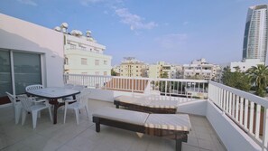 Un balcon avec une table et des chaises, un banc et une vue sur les bâtiments environnants.