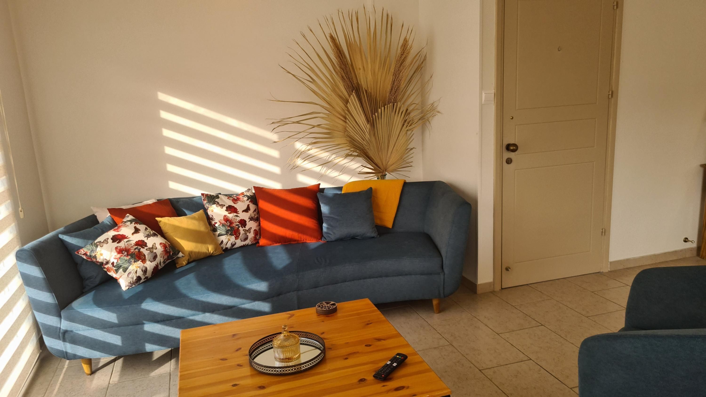 Un salon avec un canapé bleu, des coussins colorés, une table basse en bois et une grande plante décorative.