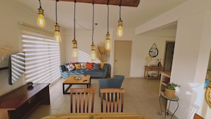 A living room with a sofa, coffee table, and chairs, a TV, and hanging light fixtures. - 83 Lim2 - Stay Naturaleza Penthouse (Limassol)