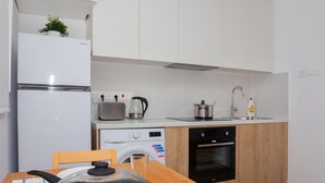 Een moderne keuken met witte kastjes, een ingebouwde oven, een spoelbak en een eettafel met een pan erop.