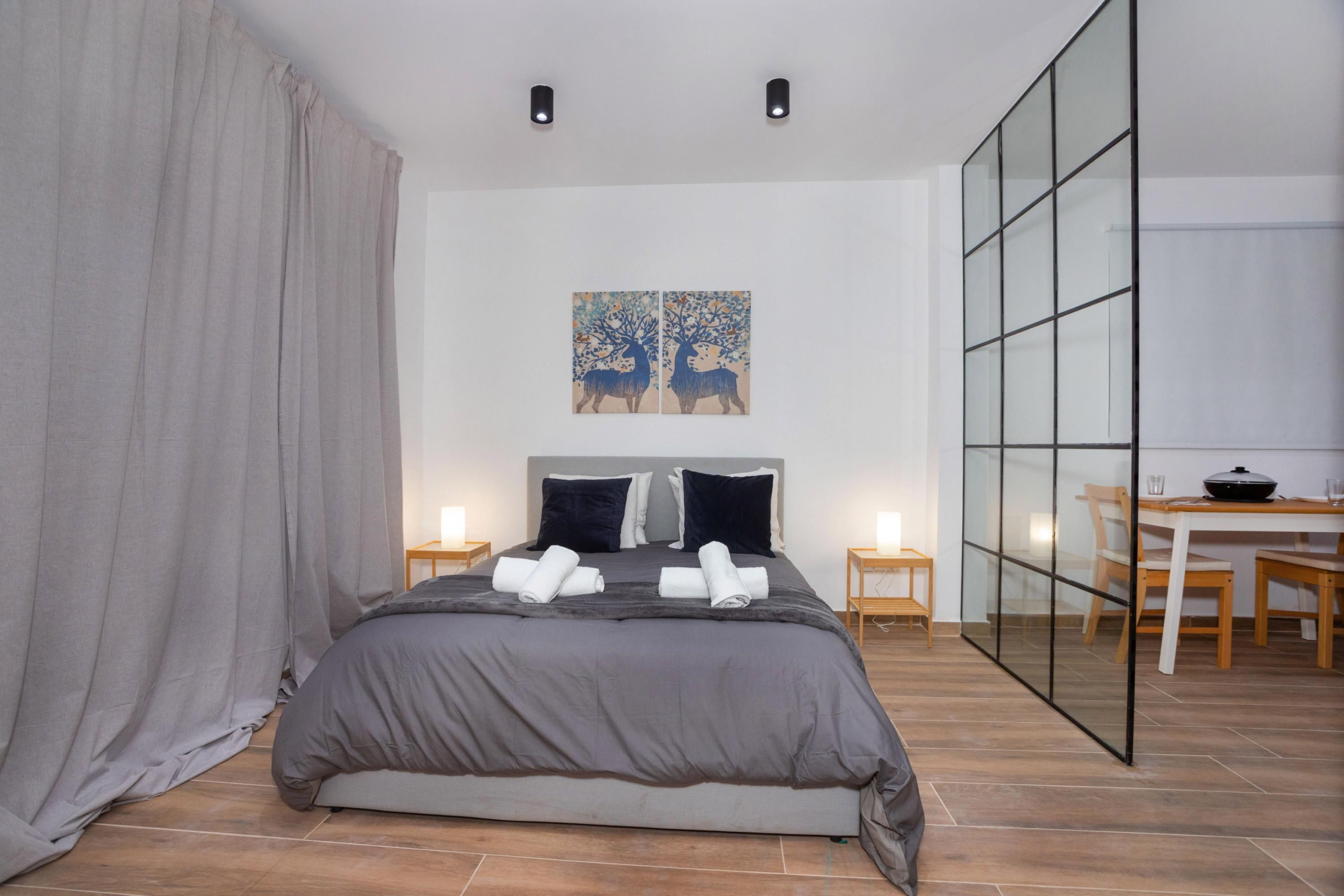 A modern bedroom with a large bed, a glass partition wall, and a dining area with a table and chairs.
