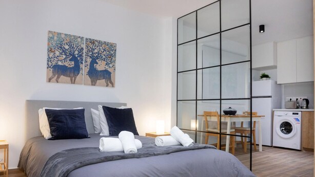Een moderne slaapkamer met een groot bed, een tafeltje en een wasmachine in de aangrenzende ruimte.