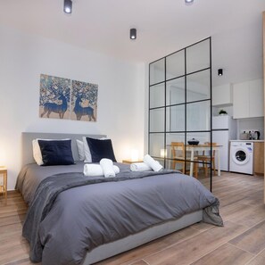 A modern bedroom with a large bed, a small table, and a washing machine in the adjacent room. - 89 LIM - Stay Zen Studio (Limassol)