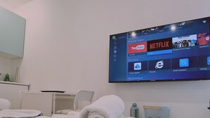 Ένα δωμάτιο ξενοδοχείου με ένα κρεβάτι, μια τηλεόραση τοποθετημένη στον τοίχο που προβάλλει την διεπαφή μιας υπηρεσίας ροής περιεχομένου και ένα μικρό τραπέζι με ένα μπουκάλι και ένα ποτήρι.