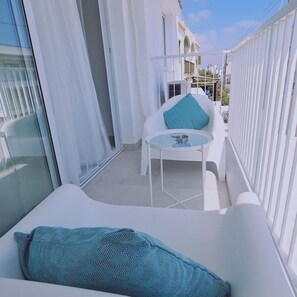 Un balcón con un sofá blanco, una mesita y una silla con cojín azul.