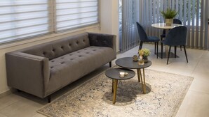 Un salon moderne avec un canapé gris, une petite table ronde ornée d’une bougie et un tapis à motifs.