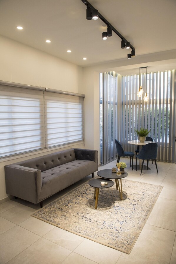 Un salon moderne avec un canapé gris, une table ronde entourée de chaises, un petit tapis et une plante en pot.
