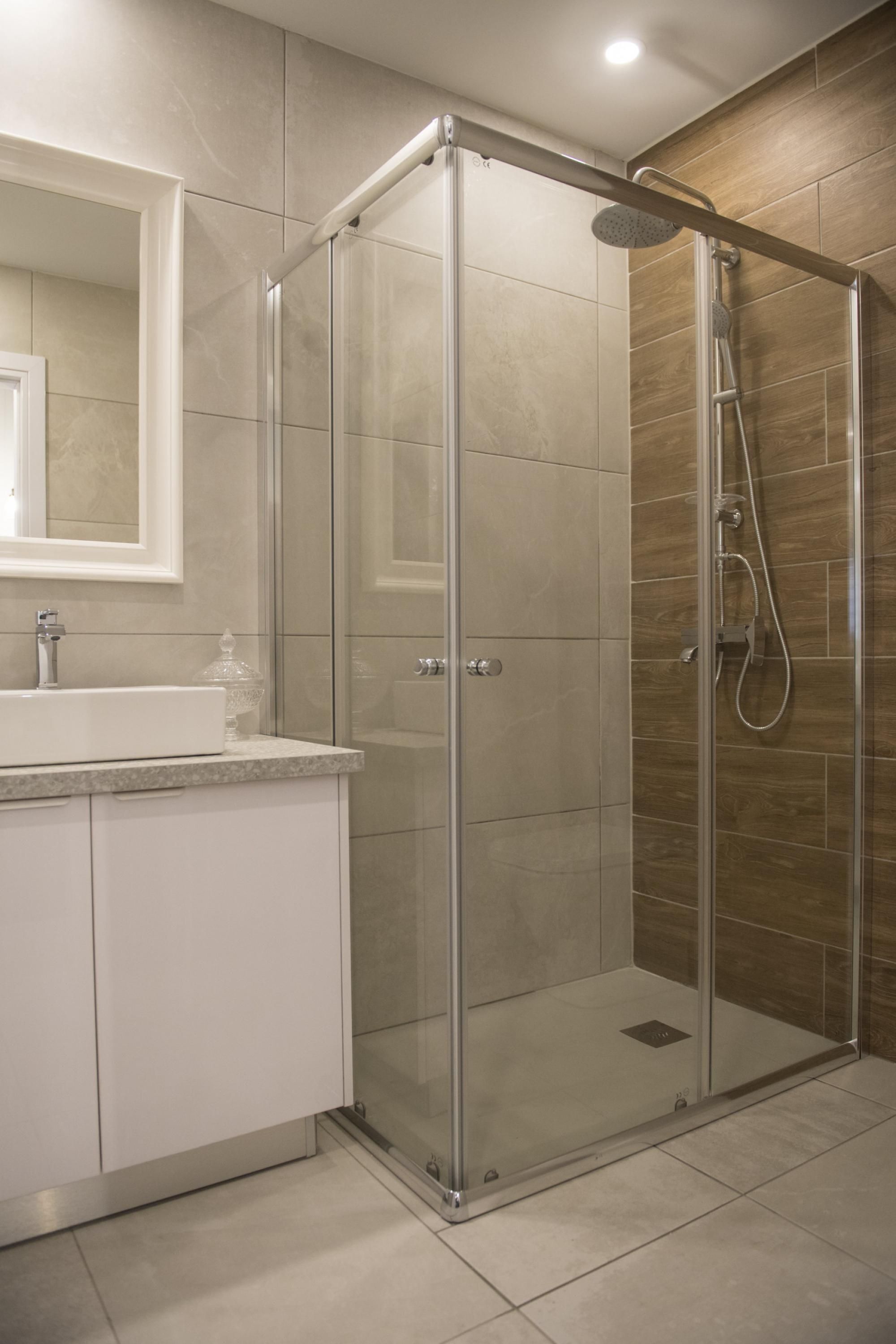 Un baño moderno con ducha envuelta en vidrio, un lavabo blanco y un espejo grande.