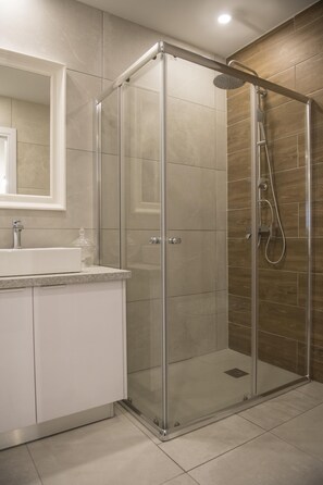 Ein modernes Badezimmer mit einer Duschkabine, einem weißen Waschbecken und einem großen Spiegel.