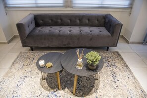 A grey sofa, two round tables with black tops and gold legs, a patterned rug, and a potted plant. - 96 Nic1 - Stay Glam Skin Studio (Nicosia)