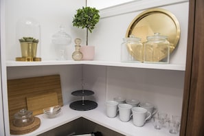 Uma prateleira com diversos objetos de vidro, incluindo um jarro de cristal, um vaso rosa e uma pequena planta em vaso.