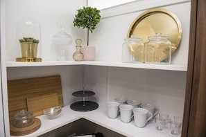 A shelf with various glassware, including a crystal decanter, a pink vase, and a small potted plant. - 96 Nic1 - Stay Glam Skin Studio (Nicosia)