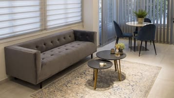 Una sala de estar moderna con un sofá gris, una mesa redonda con sillas, una alfombra pequeña y una planta en maceta.
