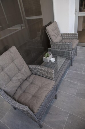 A wicker sofa set with a glass-top coffee table, a small potted plant, and a white bowl. - 96 Nic1 - Stay Glam Skin Studio (Nicosia)