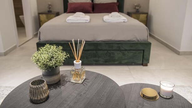 A neatly made bed with two pillows, a bedside table with a potted plant, a candle, and a glass candle holder. - 96 Nic1 - Stay Glam Skin Studio (Nicosia)