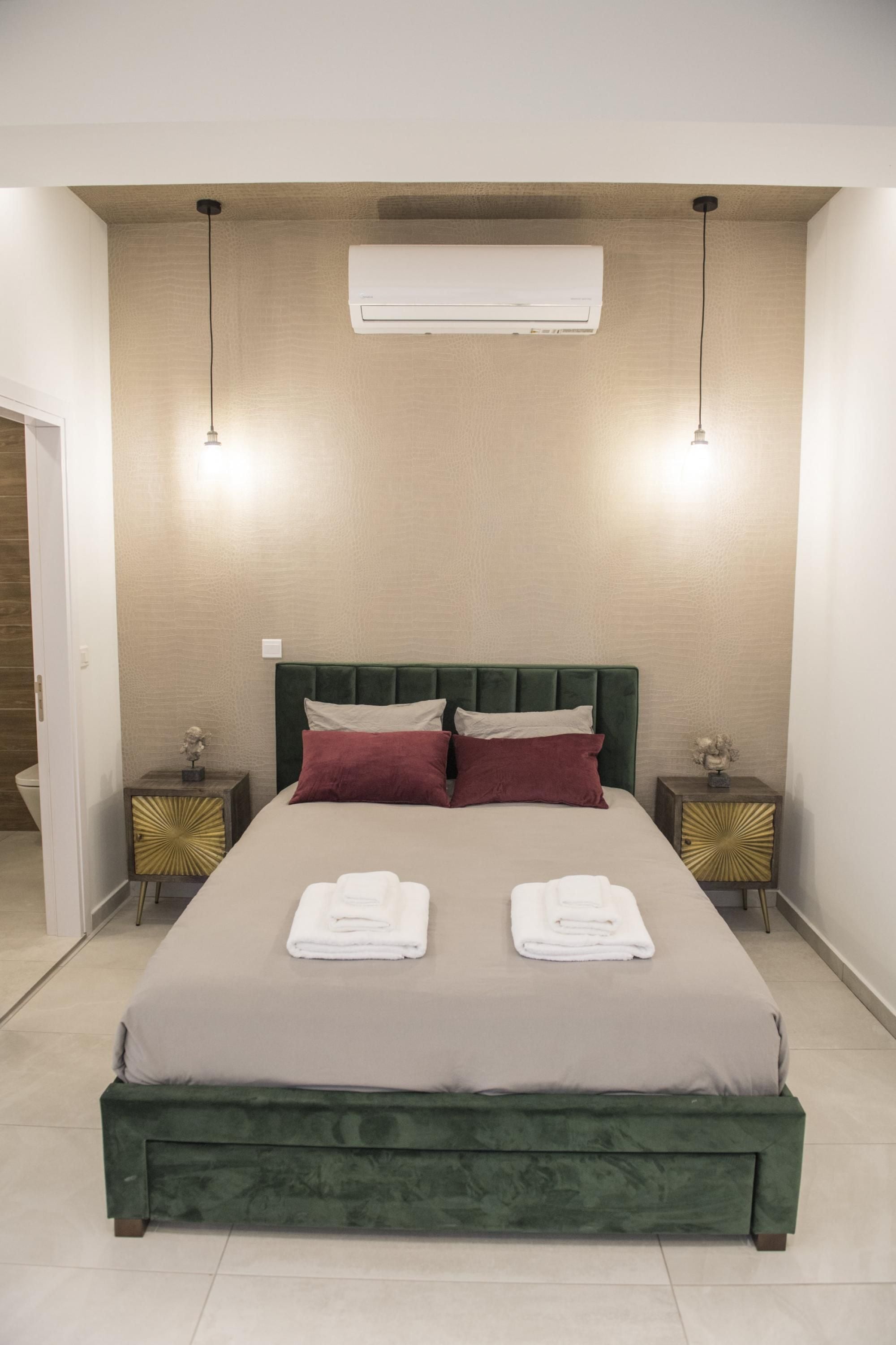 A hotel room with a large bed, two bedside tables, an air conditioning unit, and a door.