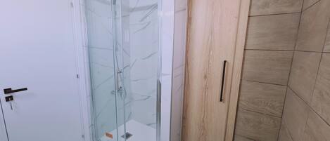 A bathroom with a glass shower enclosure, a wooden door, and tiled walls.