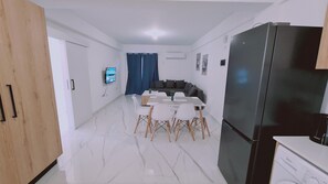 Eine moderne Küche mit einem schwarzen Kühlschrank, ein Essbereich mit weißem Tisch und Stühlen sowie eine Wohnbereich mit einem dunkelgrauen Sofa.
