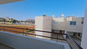 Un edificio residencial con balcón, un área pavimentada en frente y cielo despejado.