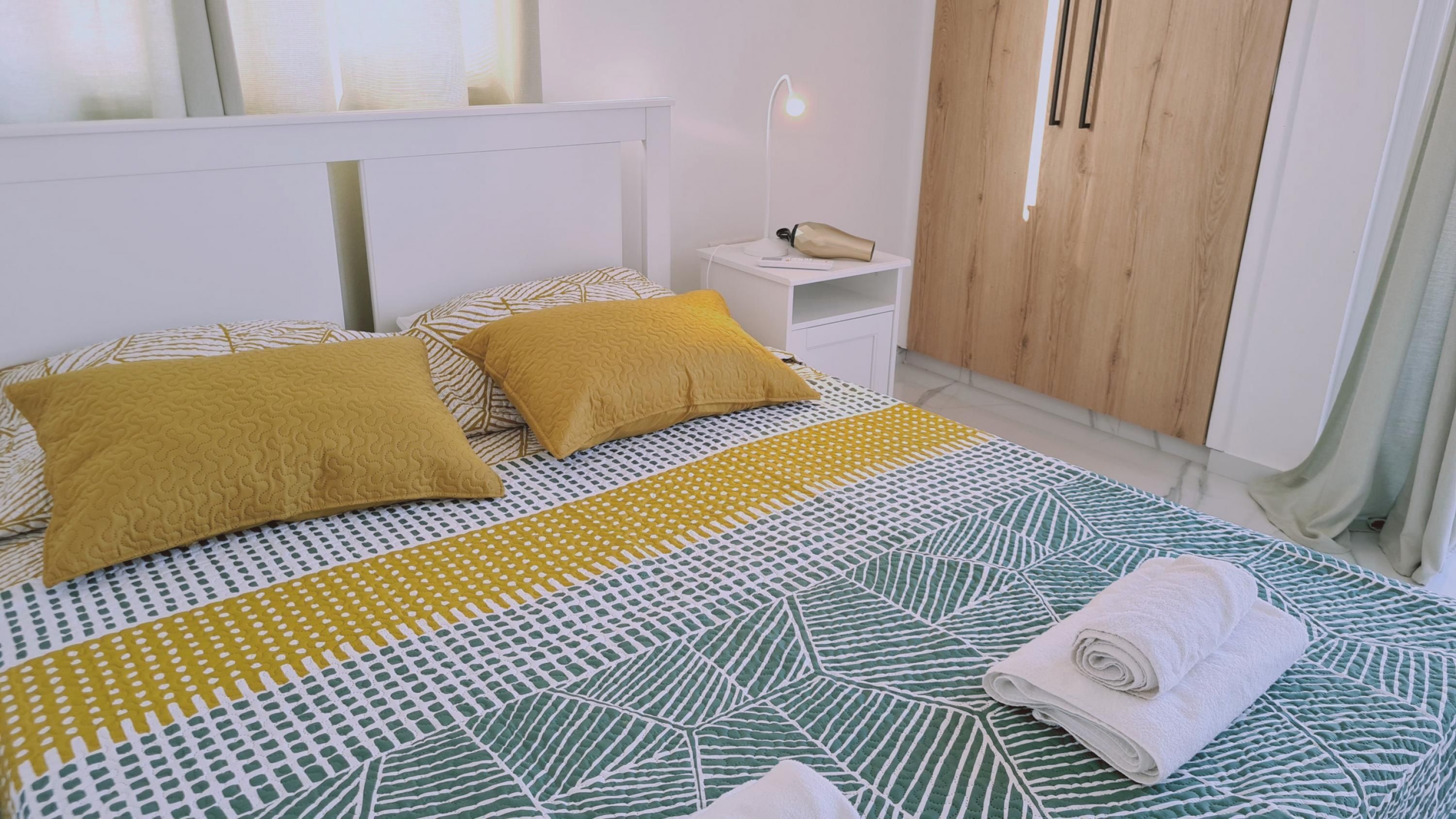 A neatly made bed with patterned bedding, a bedside lamp, and a rolled towel on the side.