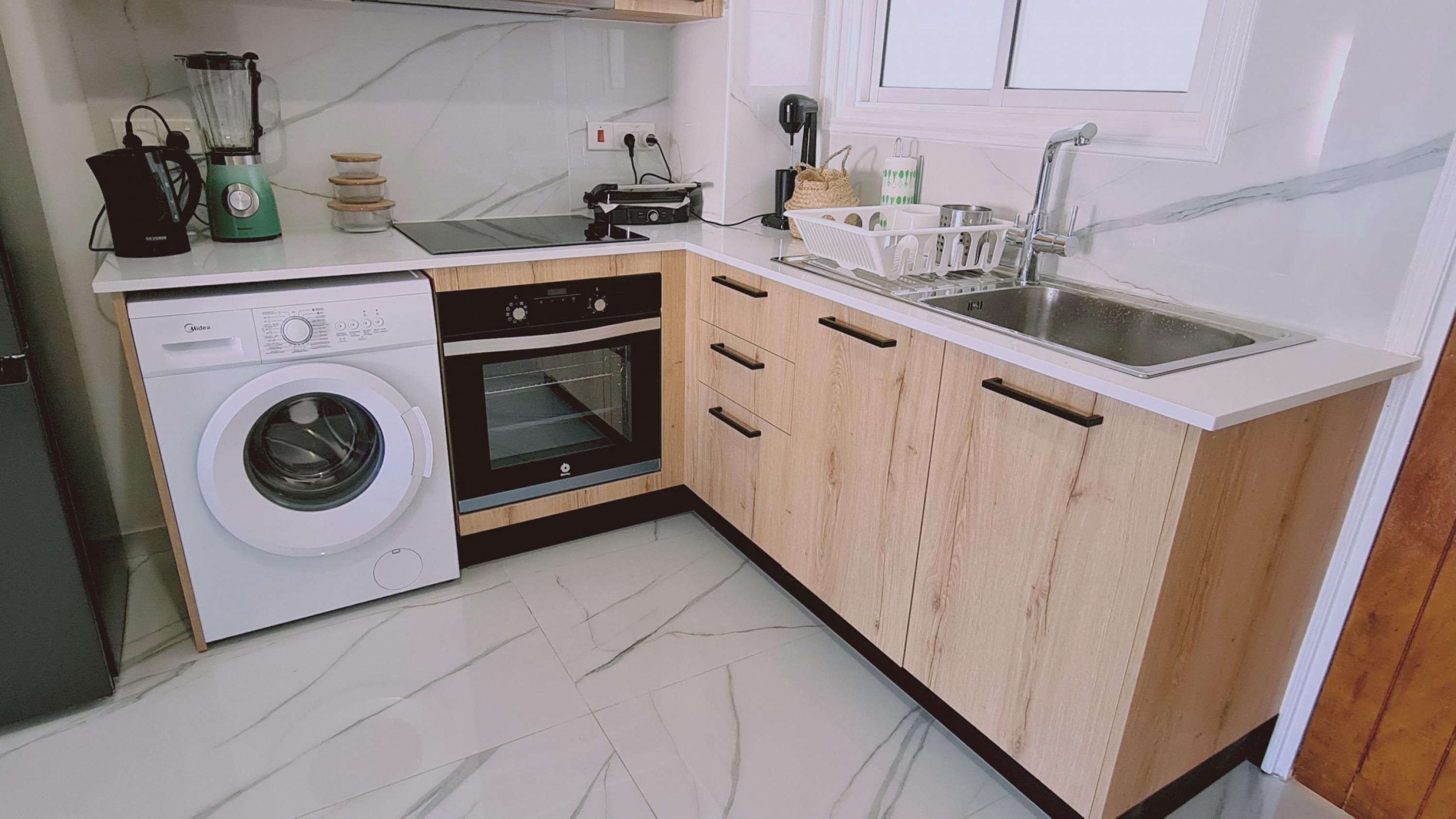 Een compacte keuken met een wasmachine, oven en een spoelbak met een moderne kraan.