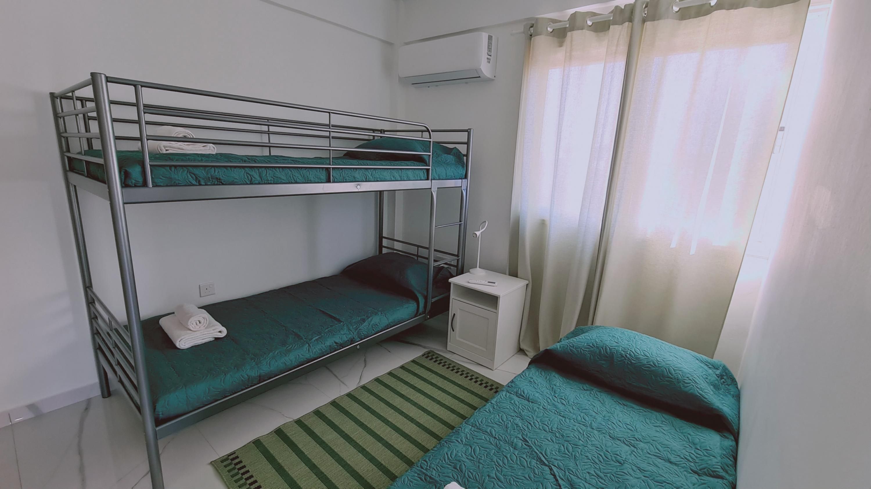 A bunk bed room with a small desk and a window with curtains.