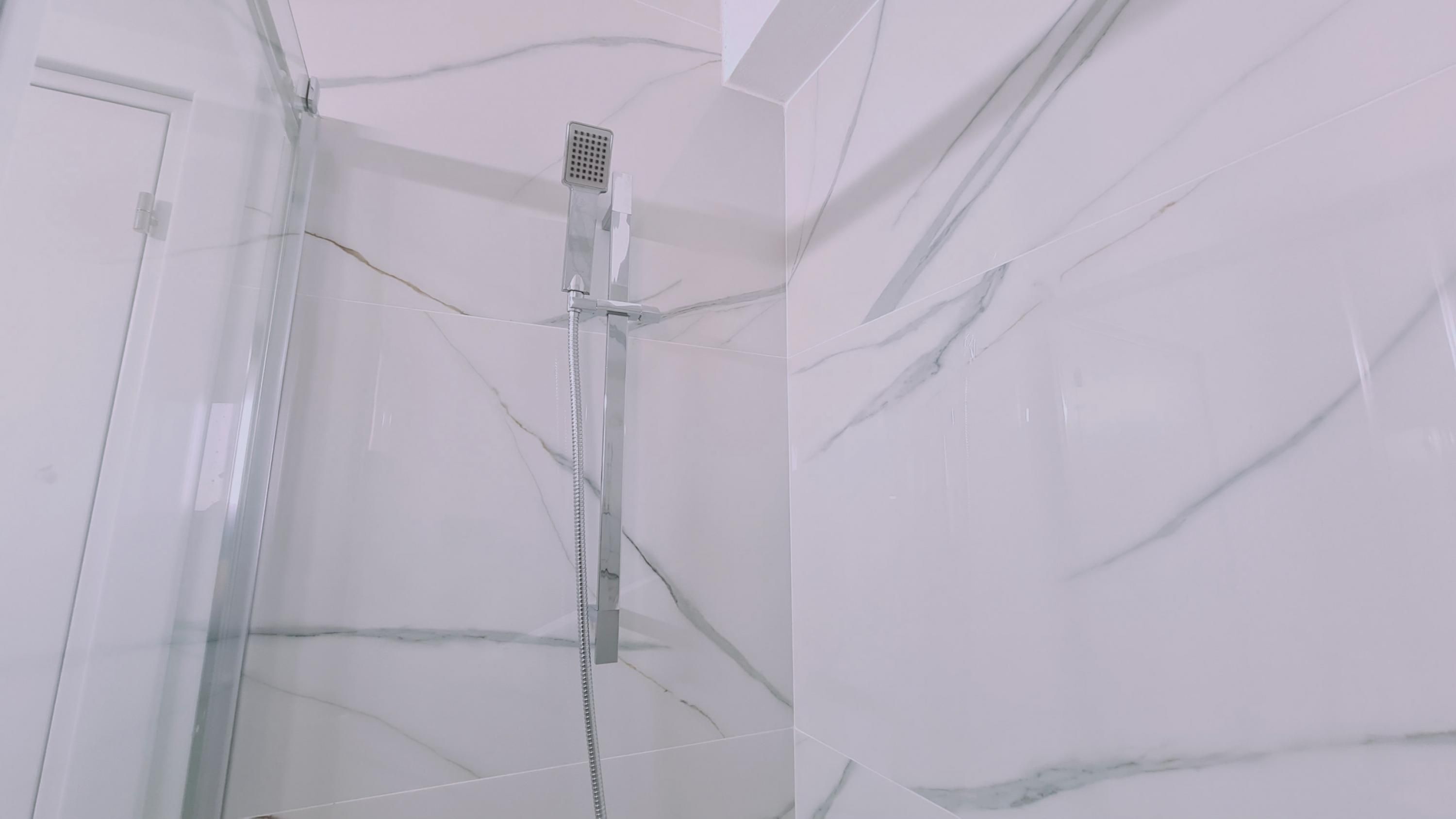 Een badkamer met witte marmeren wanden en een douchecabine van glas.