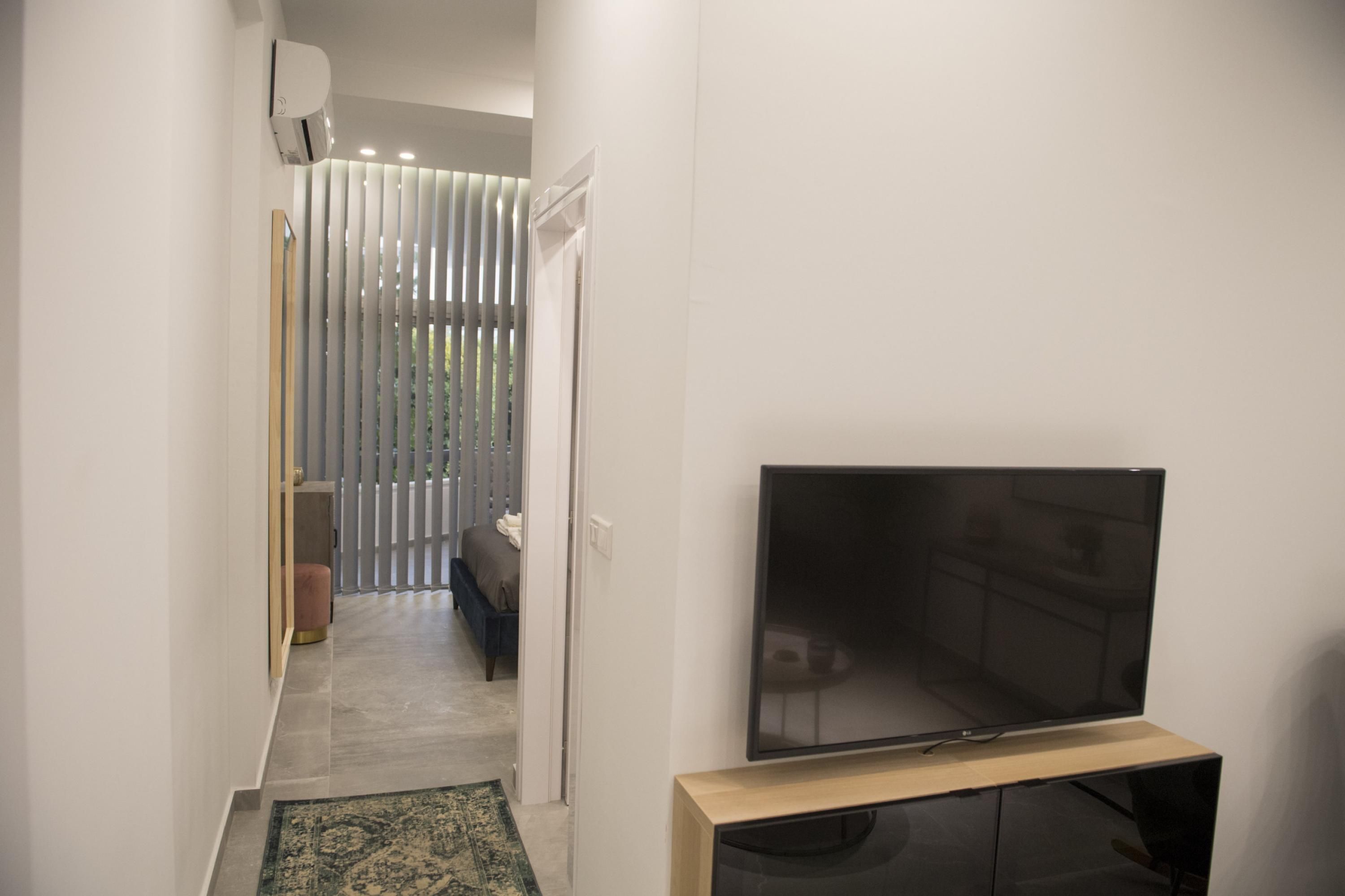 A hallway with a flat-screen TV on a wooden stand, a bench, and a patterned rug.