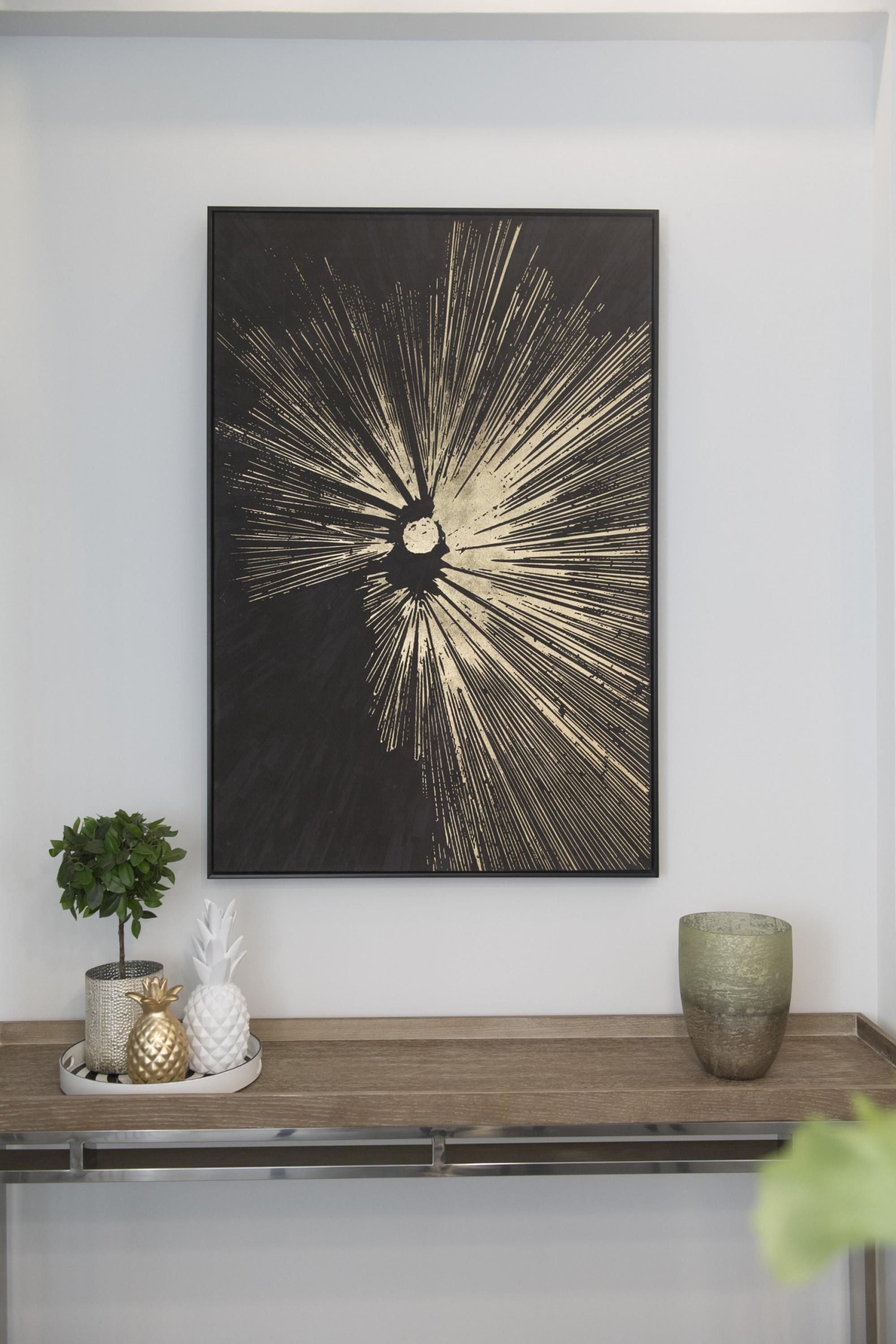 A black and gold abstract artwork on a wall, a small potted plant, and decorative pineapple-shaped items on a wooden shelf.